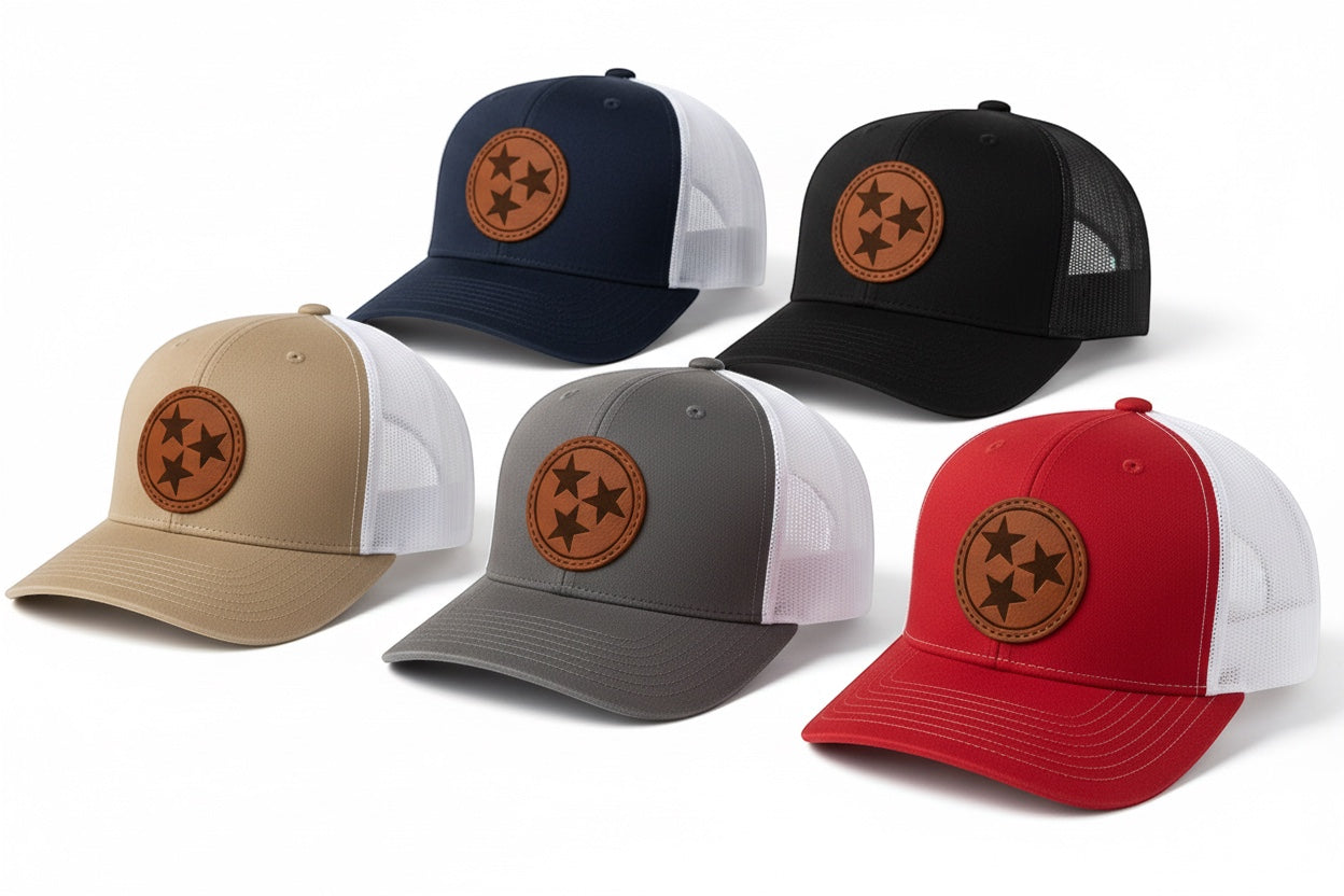 Press Society Tristar Trucker Hat in navy, black, tan, grey, and red with embroidered patch and mesh back. Adjustable snapback.